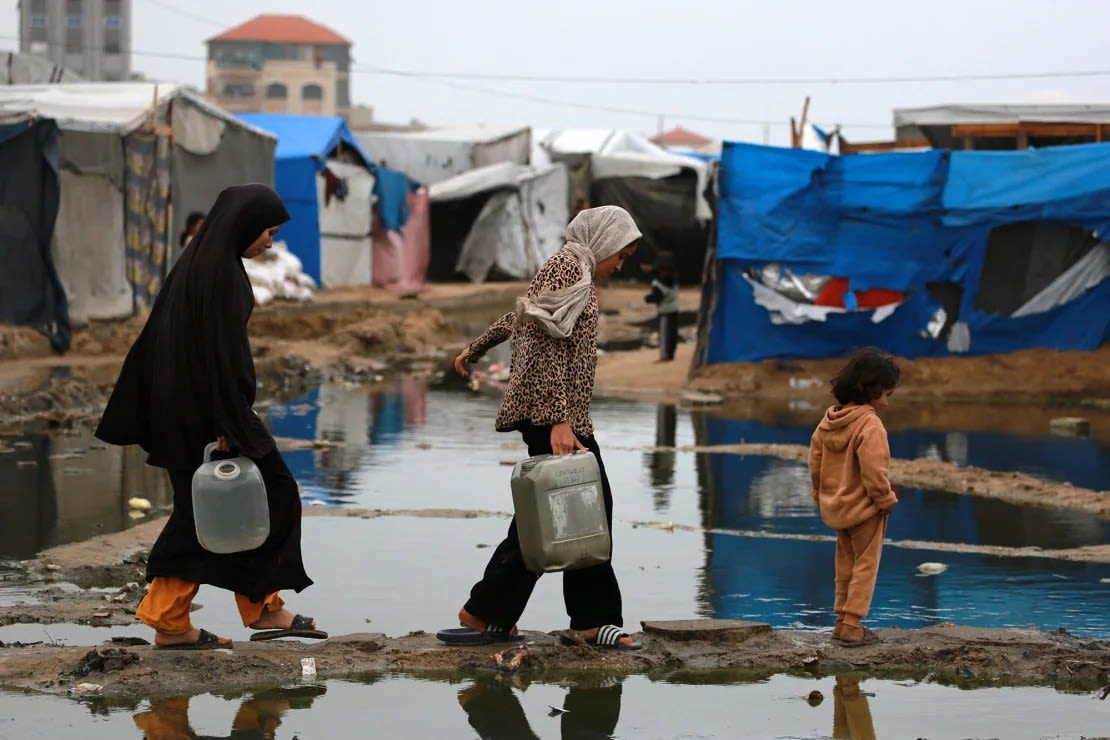 Mujeres palestinas desplazadas llevan agua a su tienda de campaña al norte de Deir el-Balah en Gaza el domingo.