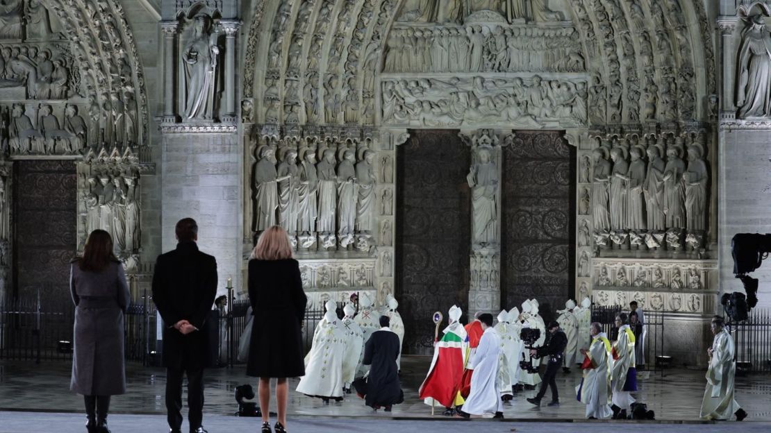 Poco después del atardecer, la alcaldesa de París, Anne Hidalgo, a la izquierda, el presidente de Francia, Emmanuel Macron, y su esposa Brigitte Macron se encuentran en el atrio renovado mientras el arzobispo de París, Monseñor Laurent Ulrich, lidera una procesión de arzobispos, obispos y sacerdotes hacia las puertas de la catedral al inicio de la ceremonia.