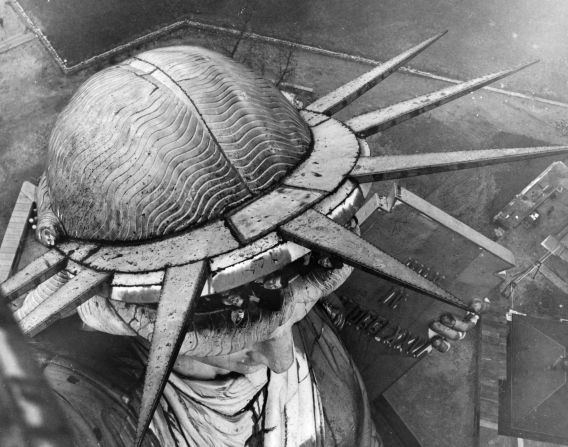 1930: Un grupo de personas observan al fotógrafo mientras captura, desde las alturas, la corona de la Estatua de la Libertad.