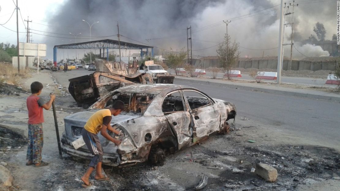 La amenaza terrorista de ISIS: dos niños detrás de un vehículo quemado observan los enfrentamientos entre las fuerzas de seguridad iraquíes y militantes de ISIS en Mosul.