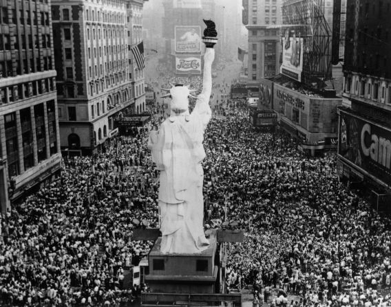 Multitudes se agrupan en la Gran vía Blanca, en Nueva York, luego de que el presidente Truman anunciara que Japón se había rendido en la Segunda Guerra Mundial. Una réplica a menor escala de la Estatua de la Libertad en el centro de la imagen.