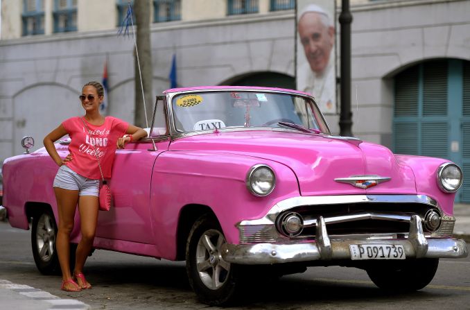 Una turista posa junto a un taxi, en La Habana, horas antes de la llegada del papa Francisco. Carteles con la foto del pontífice se pueden ver por las principales avenidas y calles de la capital cubana.