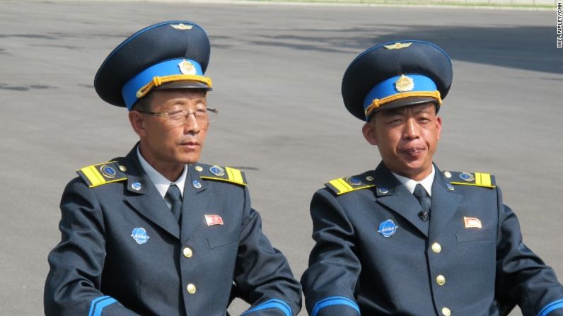 Los dos principales científicos del centro espacial vestidos con sus nuevos uniformes. En el lado izquierdo tienen un prendedor con los retratos de los exlíderes Kim Il Sung y su hijo Kim Jong Il. En el lado derecho, el logo de la agencia, que se parece al de la NASA.