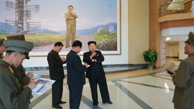 Kim Jong Un frente a una pintura enorme de su padre y exlíder, Kim Jong Il, junto a un satélite dentro del centro espacial.