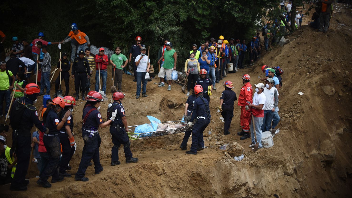 Bomberos guatemaltecos transportan un cadáver recuperado de entre la tierra que produjo un alud en la aldea El Cambray II.