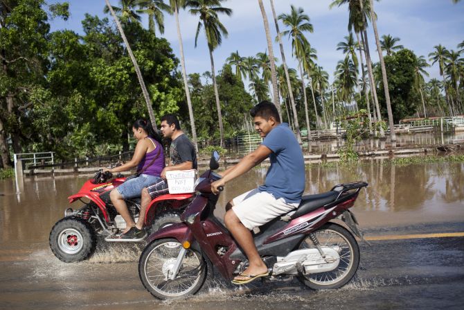 Residentes de Cihuatlán, Jalisco, pasan en sus motocicletas por una avenida con encharcamientos que dejaron las lluvias del huracán Patricia.