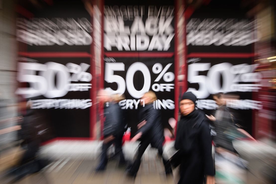 Varias personas pasan por una tienda en Londres que anuncia grandes descuentos por el llamado "viernes negro".