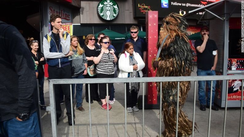 Un grupo de peatones observa mientras una persona vestida como Chewbacca se une a la fila de fanáticos a las afueras del teatro.