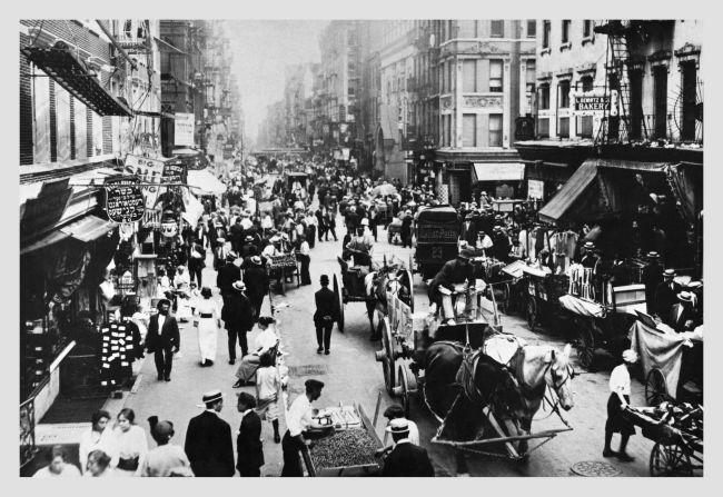 Caballos tiran de carruajes entre los vendedores ambulantes y los peatones en el Lower East Side en la década de 1900.