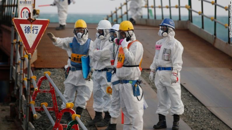 Trabajadores, con trajes y máscaras de protección, de pie cerca de los edificios de los reactores No. 3 y No. 4.