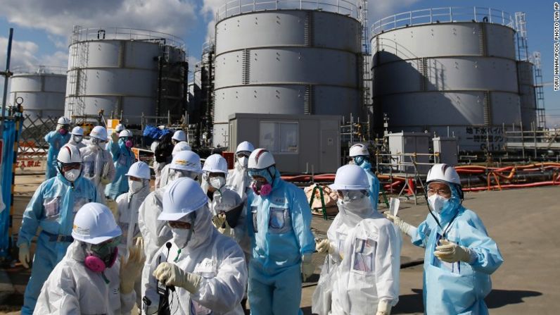 Empleados de TEPCO, con trajes protectores azules, instruyen a un grupo de prensa delante de los tanques de almacenamiento para agua radiactiva