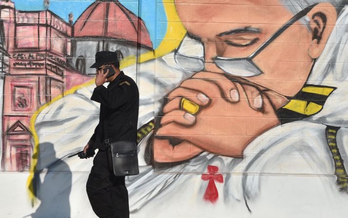 Un miembro de seguridad habla por teléfono cerca a un mural del papa Francisco, en Ecatepec.