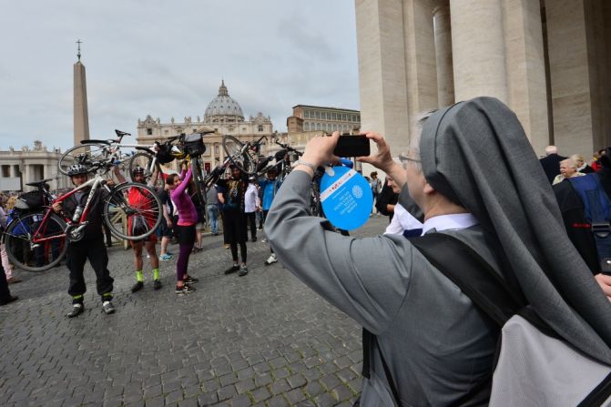 Una monja toma una fotografía de la gente que se reúne en la plaza de San Pedro el 26 de abril de 2014, en El Vaticano, un día antes de la canonización de los Papas Juan XXIII y Juan Pablo II.