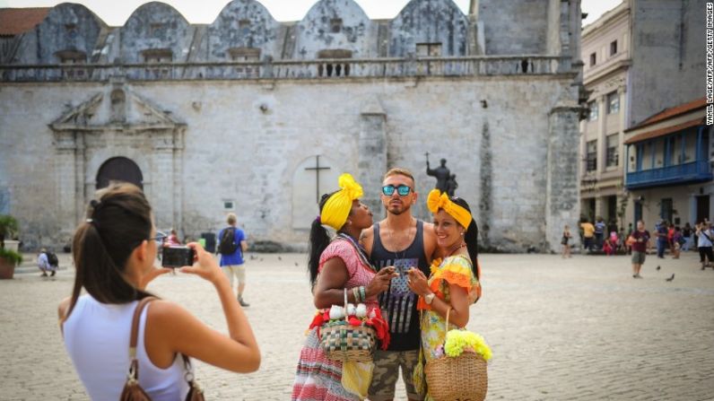 Un turista estadounidense posa entre dos cubanas vestidas con vestidos de colores encendidos en La Habana Vieja.