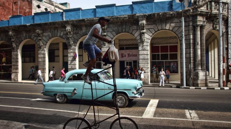 Un hombre pasa en su bicicleta modificada al lado de un auto antiguo estadounidense en La Habana.