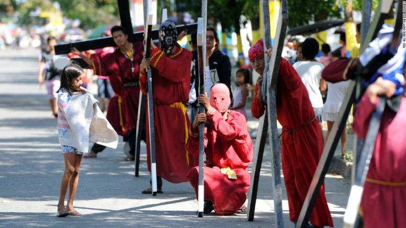 Una niña observa a nazarenos descansar luego de llevar sus cruces de madera a lo largo de una carretera de Angeles City, Pampanga.