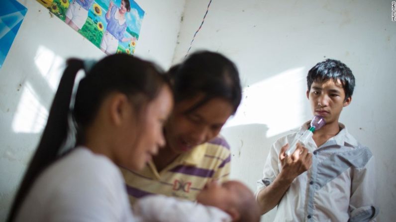 Ming sostiene un extractor de leche mientras observa a su esposa, Cai, y a su madre que cuidan a su hijo recién nacido.