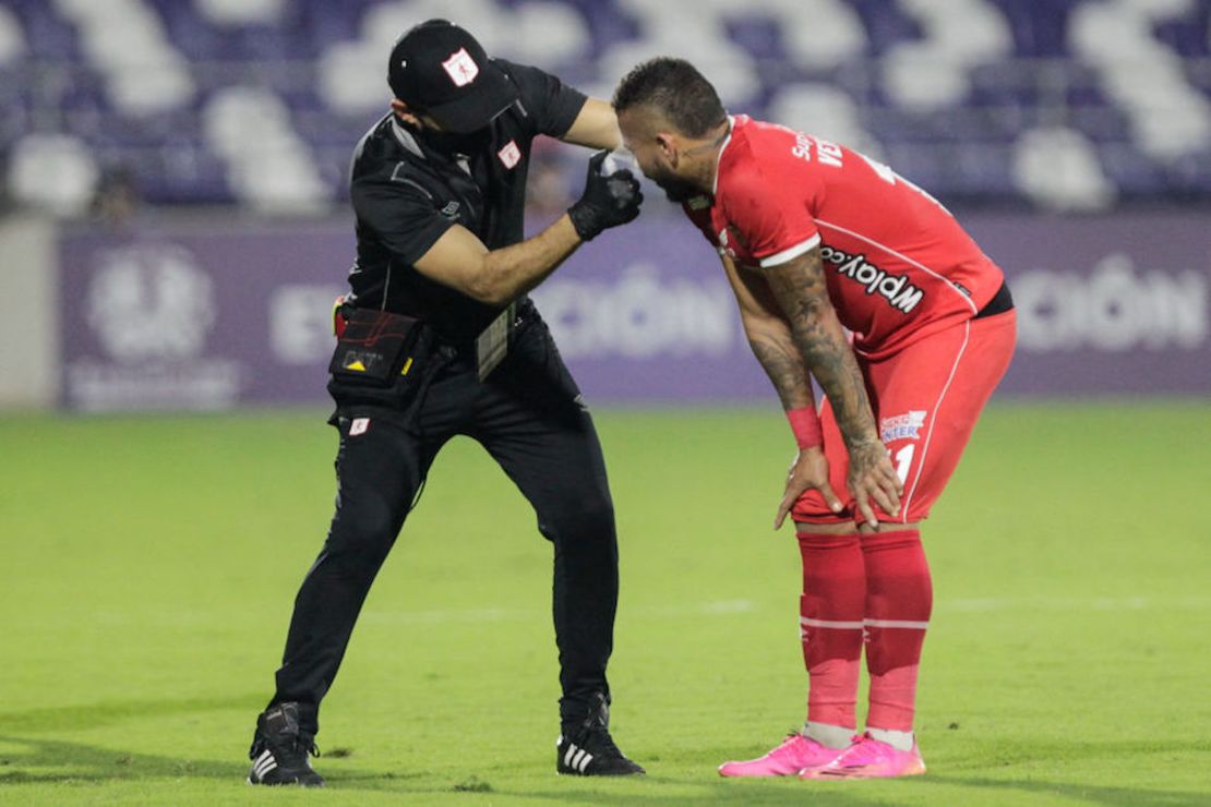 Un asistente ayuda a los jugadores afectados por gases lacrimógenos provenientes de las protestas celebradas fuera del estadio, durante el partido de la fase de grupos del torneo de fútbol Copa Libertadores entre el América de Cali de Colombia y el Atlético Mineiro de Brasil en el Estadio Romelio Martínez en Barranquilla, Colombia.