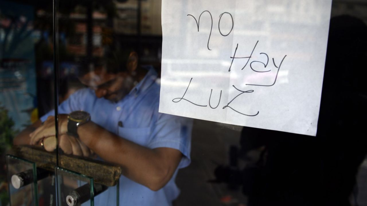 An employee of a business closed during a blackout stands behind the door with a notice reading "There's No Light", in Caracas on September 3, 2013. Major power blackouts paralyzed Venezuela's capital and several states across the country on Tuesday but there was no official explanation for the cause.  AFP PHOTO/Juan Barreto