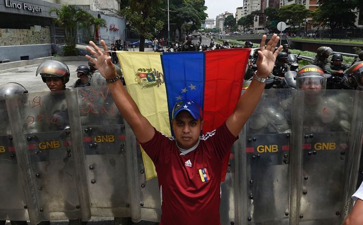 Un manifestante sostiene una bandera de Venezuela frente a una línea de policías de la GNB durante las protestas que tienen lugar días después de que el presidente Maduro decretara el estado de emergencia en ese país.