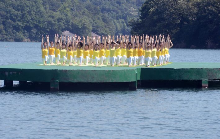 Un grupo de mujeres vestidas con una franela amarilla y pantalones blancos, realizan el asana Anjaneyasana o la postura de la luna creciente.