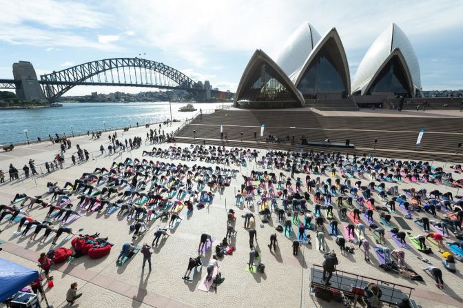 A los pies de la Casa de la Ópera de Sydney, decenas de personas realizan el Adho Mukha Svanasana, o la postura del perro boca abajo.