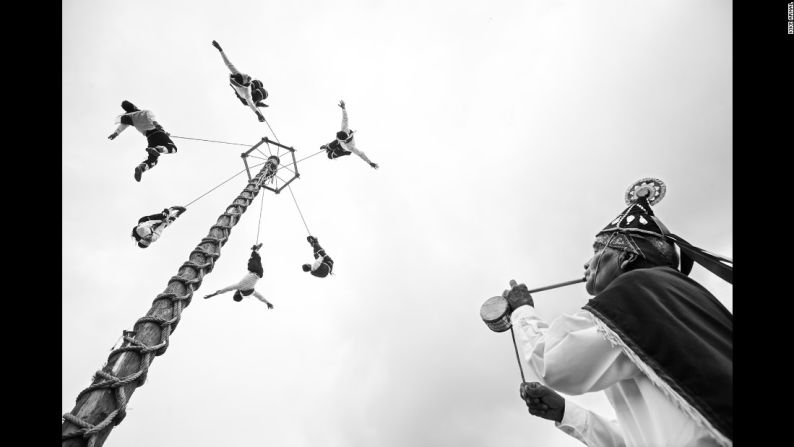 Jóvenes voladores descienden desde una vara mientras su profesor toca la flauta y el tambor.