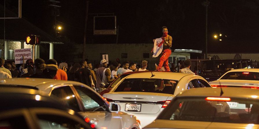 Un manifestante se para en el techo de un auto frente al lugar donde Sterling murió. El hombre de 37 años vendía discos compactos y DVDs afuera de una tienda en Louisiana.