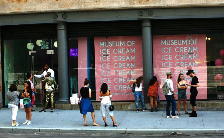 Unos visitantes posan frente a una pared llena de conos de helado.