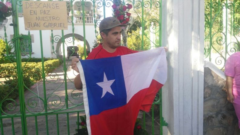 Un hombre sostiene una bandera de Chile frente a la casa de Juan Gabriel en Ciudad Juárez.