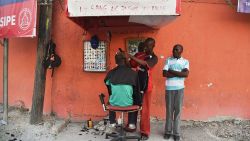 A man get his hair cut on by a barber on Delmas street in Port-au-Prince on August 22, 2016. / AFP / HECTOR RETAMAL