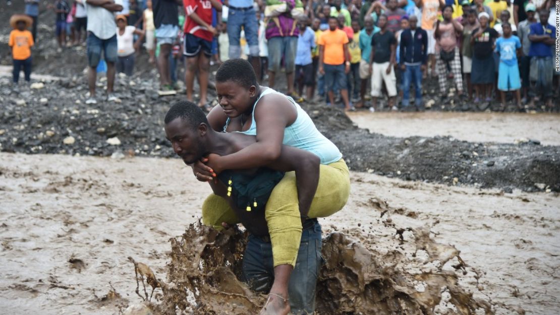 Un hombre lleva a una mujer en las espaldas a través del río Petit Goavee, en Haití, donde un puente colapsó durante las intensas lluvias del huracán Matthew.