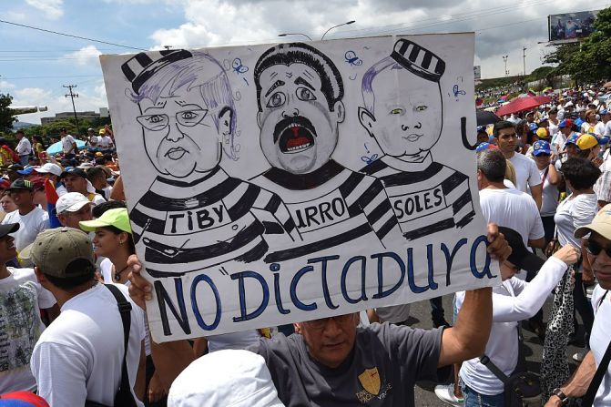 Un hombre lleva una pancarta con caricaturas de Maduro, la presidente del CNE Tibisay Lucena y Diosdado Cabello, presidente del PSUV.