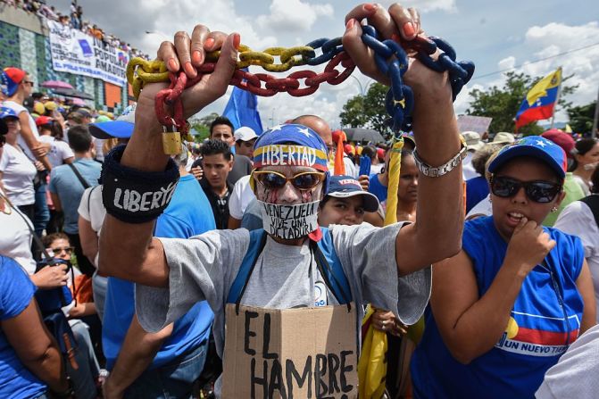 Un hombre marcha sosteniendo unas cadenas y con un letrero que dice 'el hambre'. La escasez de productos básicos en Venezuela fuerza a las personas a hacer largas filas a diario para conseguir alimentos. Algunos han reportado que están pasando hambre.