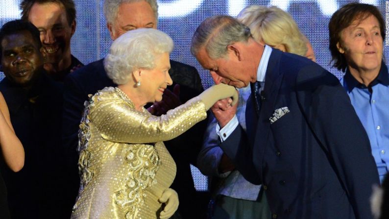 El príncipe Carlos besa la mano de su madre en la tarima mientras el cantante Paul McCartney, al fondo a la derecha, observa al público durante el concierto por el Jubileo de Diamante de la reina Isabel II, el 4 de junio de 2012, en el Palacio de Buckingham. Ese día se celebró el aniversario número 60 de la reina en el trono.