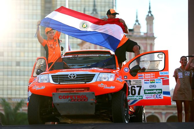 Los paraguayos Blas Zapag y Enrique Zapag sostienen su bandera durante la gala de apertura del Rally Dakar en Asunción.