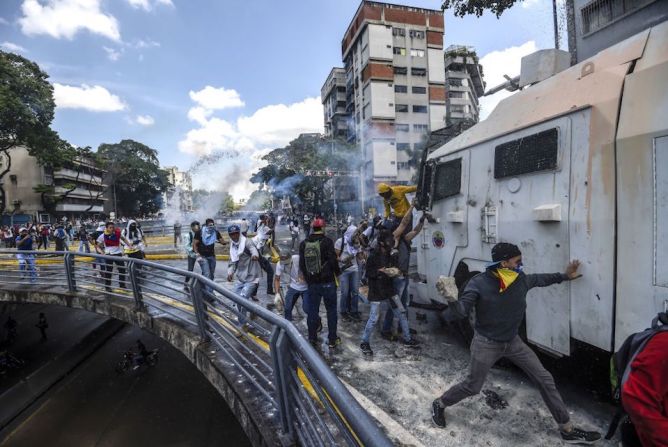 Manifestantes contra el gobierno de Nicolás Maduro atacan un vehículo de la policía antimotines.