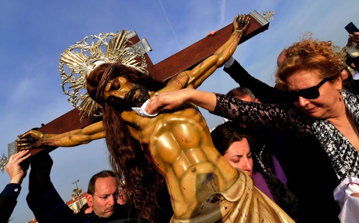 Una mujer de la hermandad Cristo Salvador, en Valencia, España, toca una efigie de Jesús en la cruz durante la procesión de Semana Santa en las playas de Valencia.