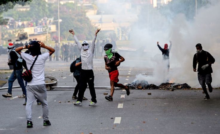 Un grupo de manifestantes camina entre una nube de gas lacrimógeno.