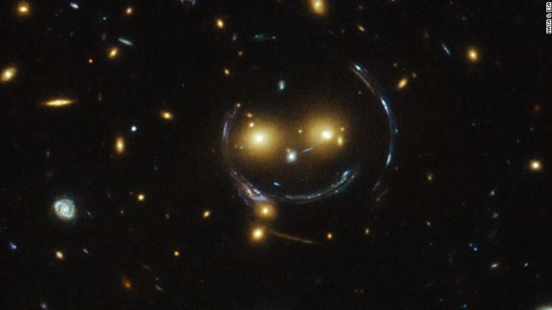 Un enorme conglomerado de galaxias conocido como SDSS J1038 + 4849 se parece a una cara sonriente en una imagen capturada por el Telescopio Hubble. Los dos ojos brillantes son en realidad dos galaxias distantes. ¿Y qué de la sonrisa y la cara redonda? Eso es un resultado de lo que los astrónomos llaman "lentes gravitacionales fuertes". Esto sucede porque la atracción gravitatoria entre los dos grupos de galaxias es tan fuerte que distorsiona el tiempo y el espacio alrededor de ellos.