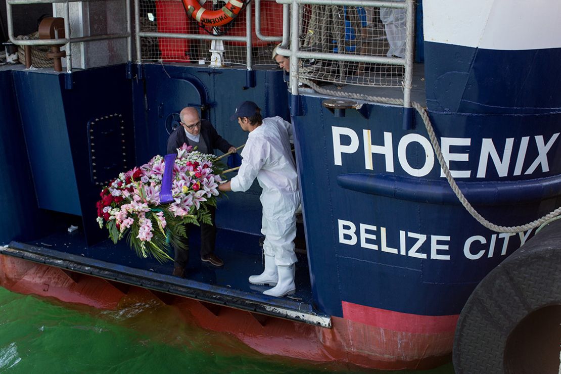 Un sacerdote, a la izquierda, y un miembro de la tripulación del Fénix dejan una corona funeraria para los inmigrantes que se ahogaron en el mar el 24 de mayo.