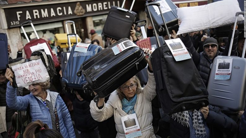 Decenas de personas sostienen maletas y letreros en protesta por el aumento los turistas que visitan Venecia, en noviembre del 2016.