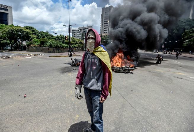 Un activista se para en frente de una motocicleta policial que arde en llamas, durante una manifestación en contra de la Asamblea Nacional Constituyente en Caracas este 30 de julio del 2017.