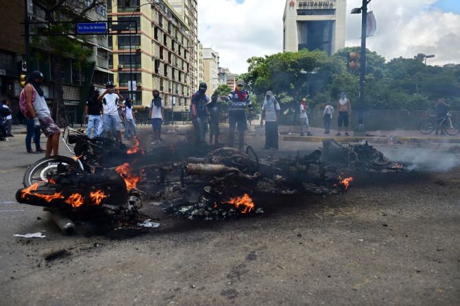 Activistas opositores observan motocicletas policiales ardientes en llamas durante una manifestación en contra de la Asamblea Nacional Constituyente en Caracas este 30 de julio del 2017.