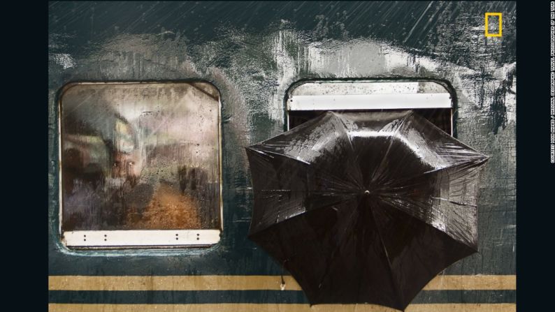 "La Mirada del Hombre". La segunda mención honorífica en la categoría de Personas es para Moin Ahmed. "La foto fue tomada el 23 de julio de 2016 en la estación de ferrocarril de Tongi, en Gazipur (Bangladesh). Estuve allí tomando fotos y esperando un momento. El tren de Dhaka hacia otro distrito había llegado y se detuvo en la plataforma durante cinco minutos para recoger pasajeros. Estaba lloviendo, de pronto encontré un par de ojos curiosos que me miraban a través de la ventana y a su izquierda un paraguas para protegerse de la lluvia.