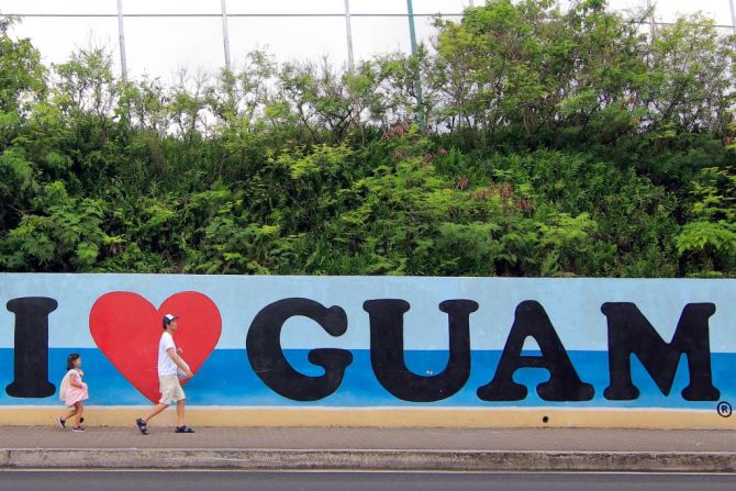 Turistas caminan frente a un muro con el eslogan "Amo a Guam" en el distrito de Tumon.