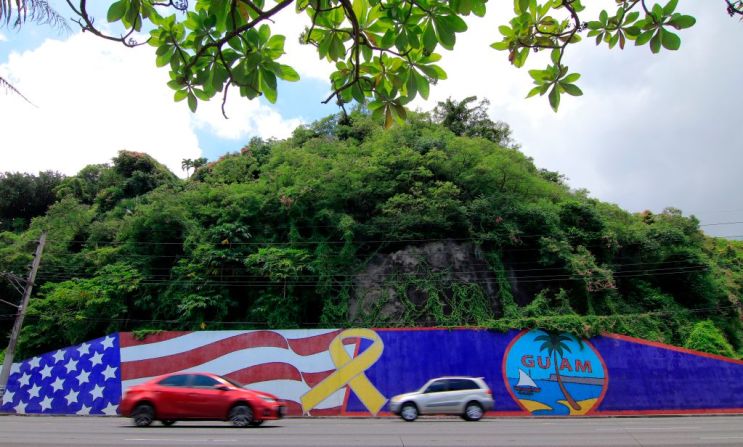 El tráfico de la tarde pasa delante de un muro pintado con las banderas de EE.UU. y de Guam en el distrito de Tumon.