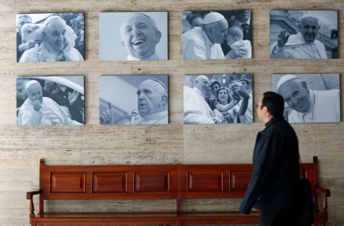 En el arzobispado de Bogotá, un hombre camina cerca de una serie de retratos del papa Francisco. Se calcula que la visita del papa deje un incremento del PIB de Bogotá de un 0,4%.