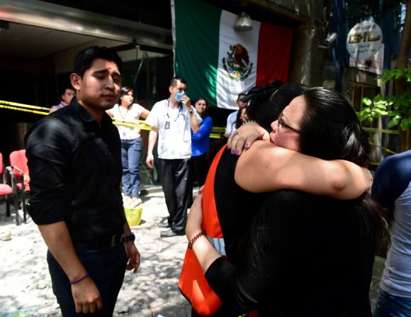 Dos mujeres se abrazan tras sobrevivir al sismo en México. Al fondo la bandera del país.