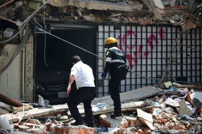 Un guardia de seguridad y un oficial de tránsito buscan posibles sobrevivientes en medio de los escombros.